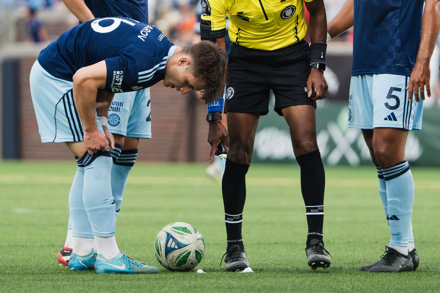 Chattanooga FC Soccer player places ball for free kick as referee stands nearby during competitive match.
