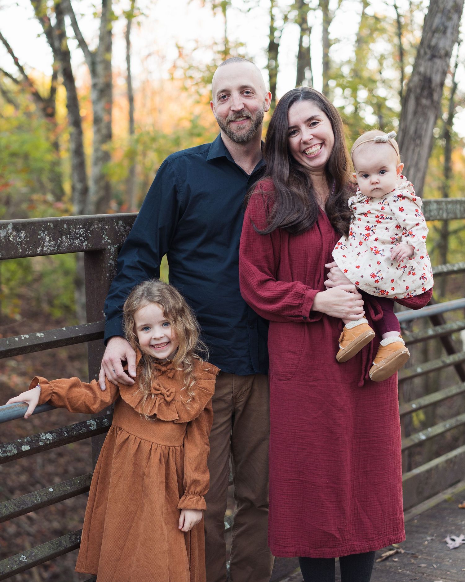 Family of four poses on wooden bridge surrounded by autumn trees in fall portrait in Chattanooga, TN.