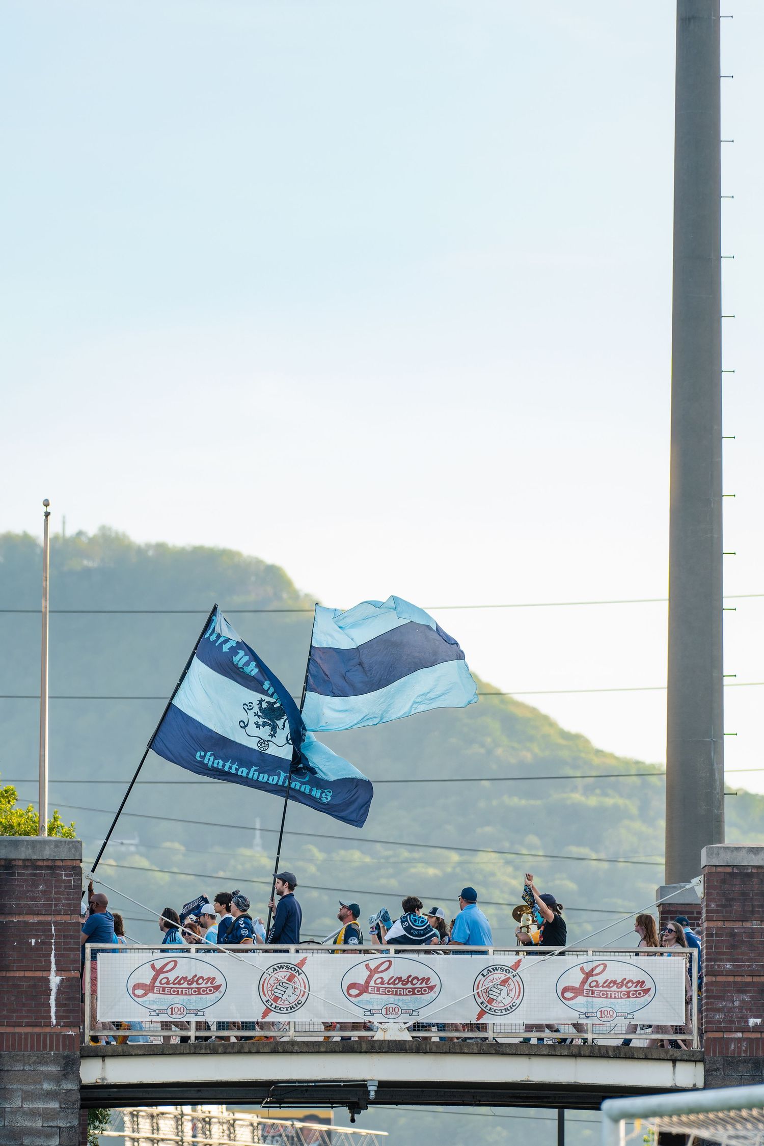 Soccer fans wave Chattanooga FC flags from a bridge before an MLS Next Pro match.
