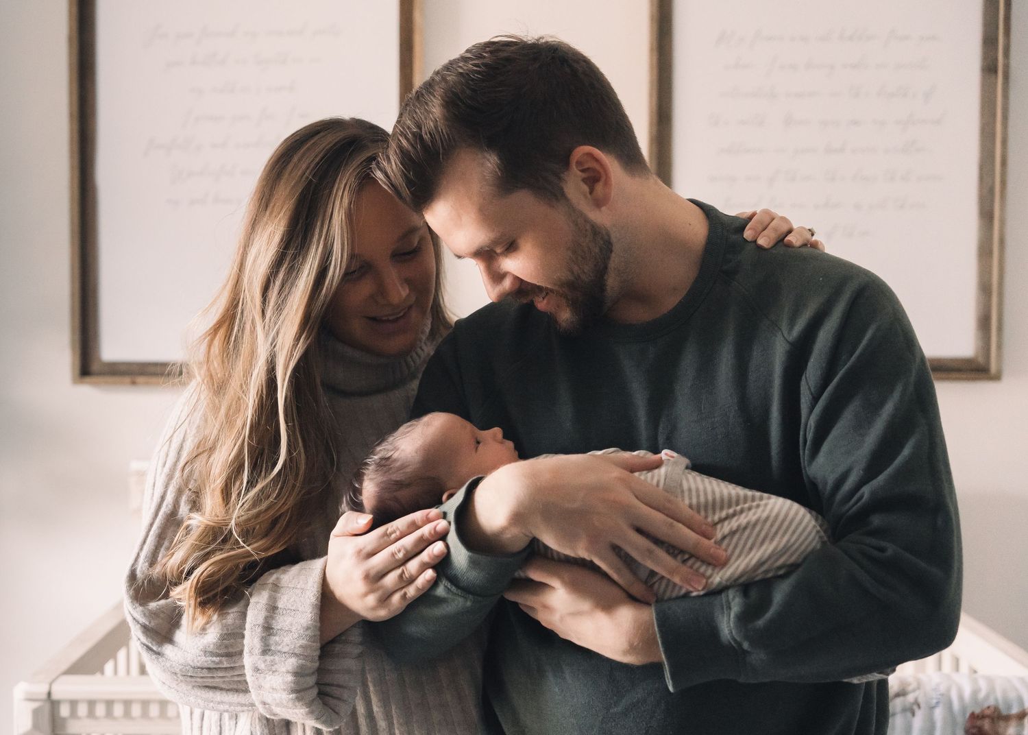 Couple tenderly cradles newborn baby together in warm indoor setting.