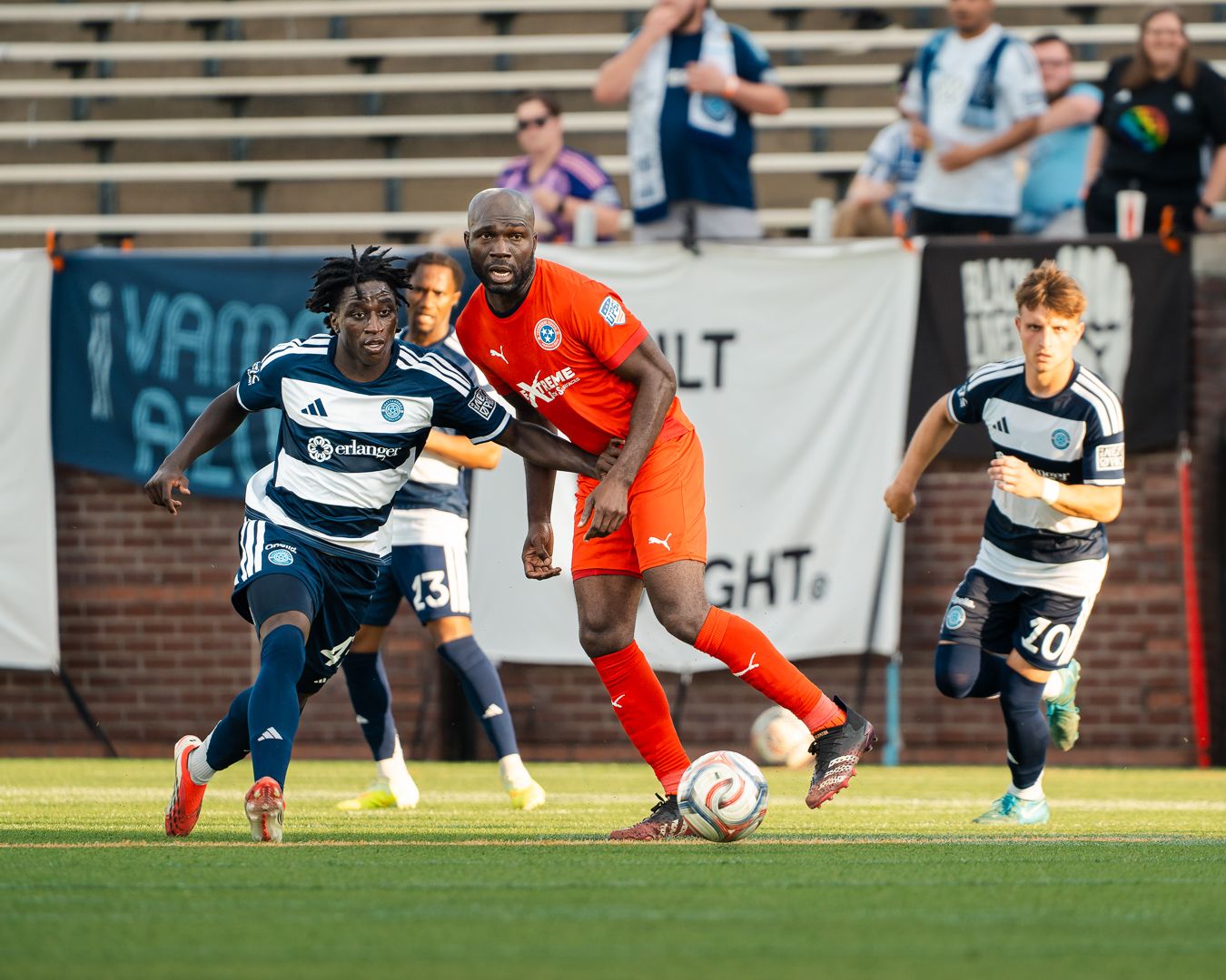 Chattanooga FC Soccer player in orange jersey dribbles ball during a MLS Next Pro league match under stadium lights at night.