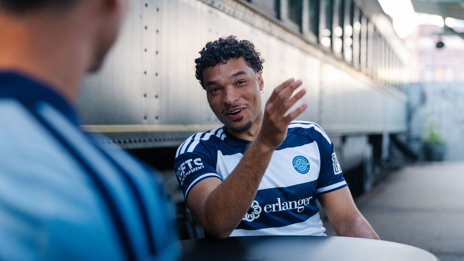 Chattanooga FC player in jersey gestures while seated near a train photographed for a creative sports assignment in Chattanooga, TN.