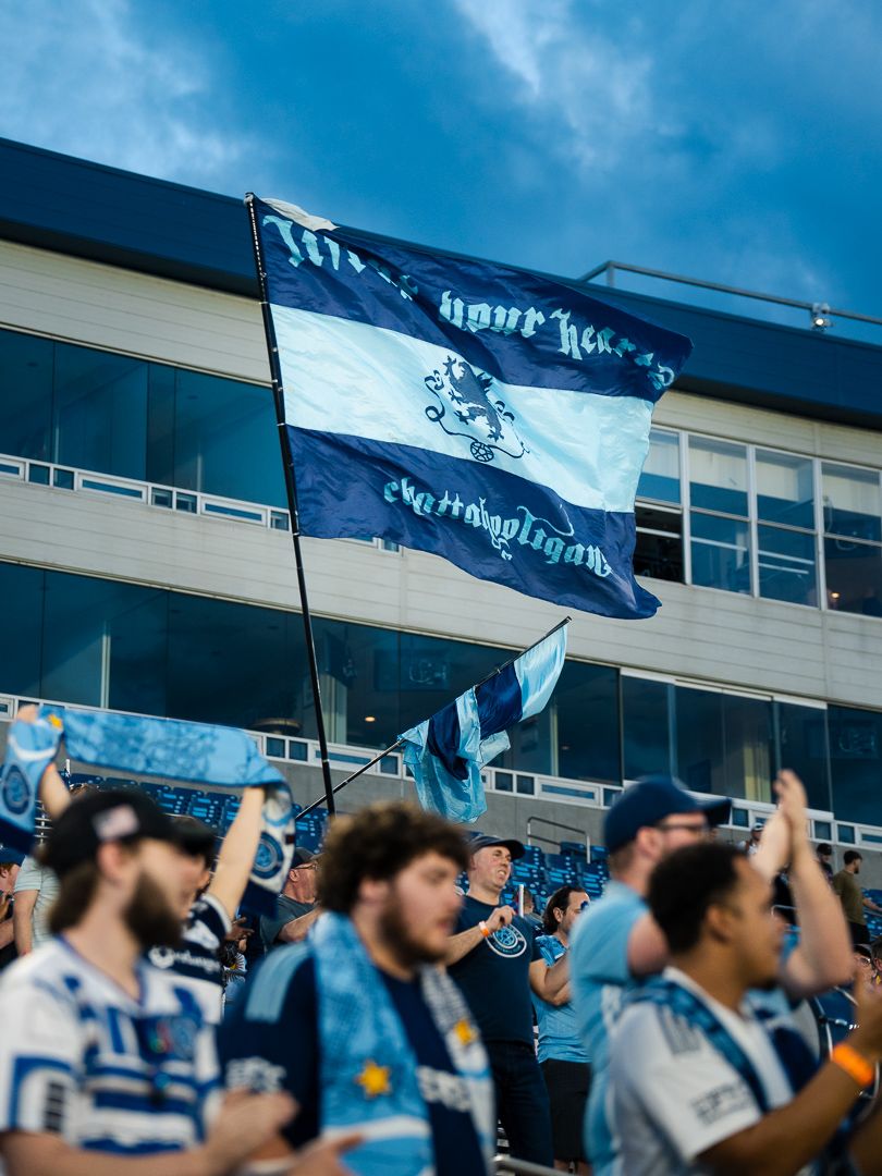 Chattanooga FC Soccer fans (Chattahooligans) wave a large navy blue banner in the supporter section during a MLS Next Pro match.