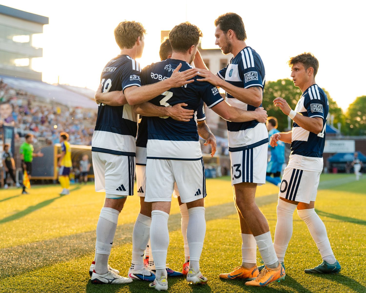 Chattanooga FC Soccer teammates celebrate together in group hug after scoring a goal during evening MLS Next Pro match.