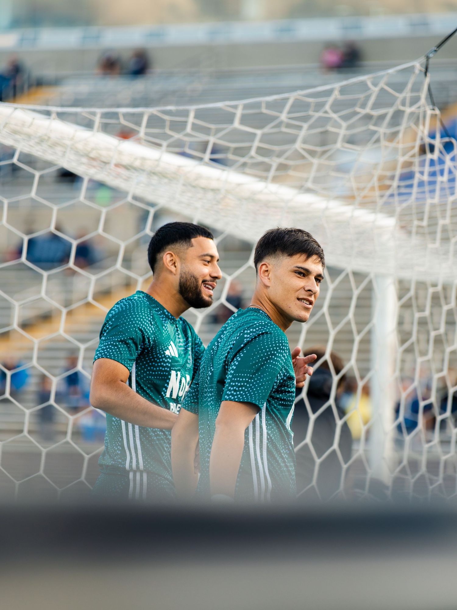 Two Chattanooga FC soccer players in teal training jerseys stand near the goal net during warmups.