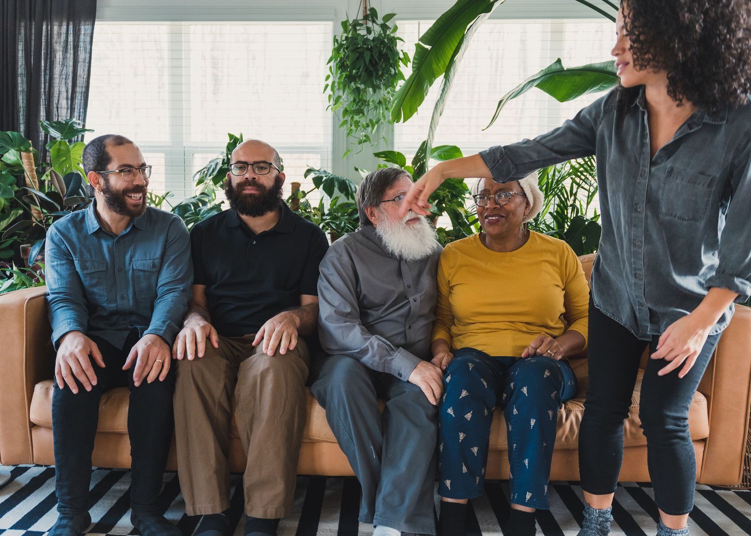 A group of five adults sit together on a couch surrounded by indoor plants.