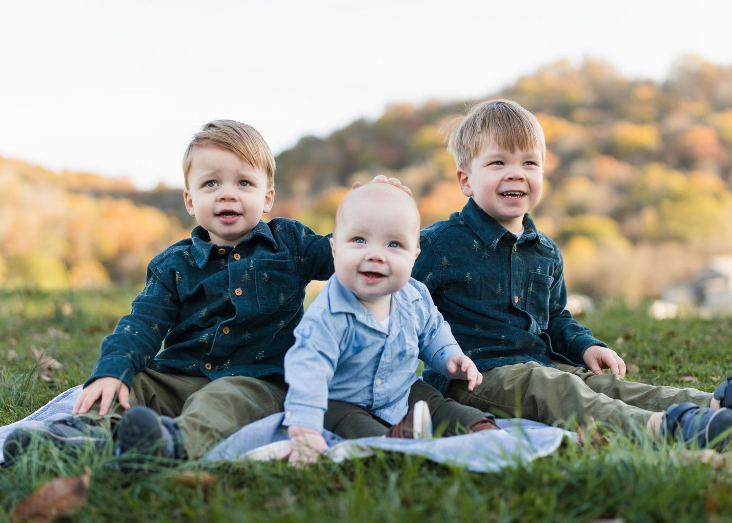 Three young brothers smile together on a blanket in a grassy field during autumn in Chattanooga, TN.