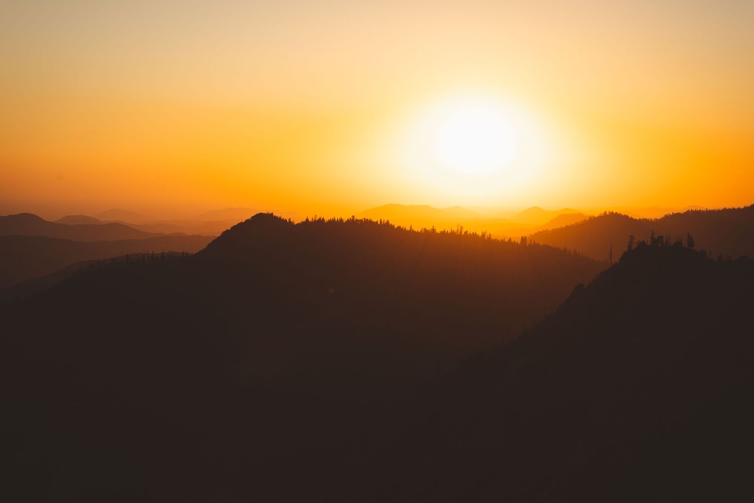 A stunning golden sunset silhouettes rolling mountain ridges in a breathtaking landscape.