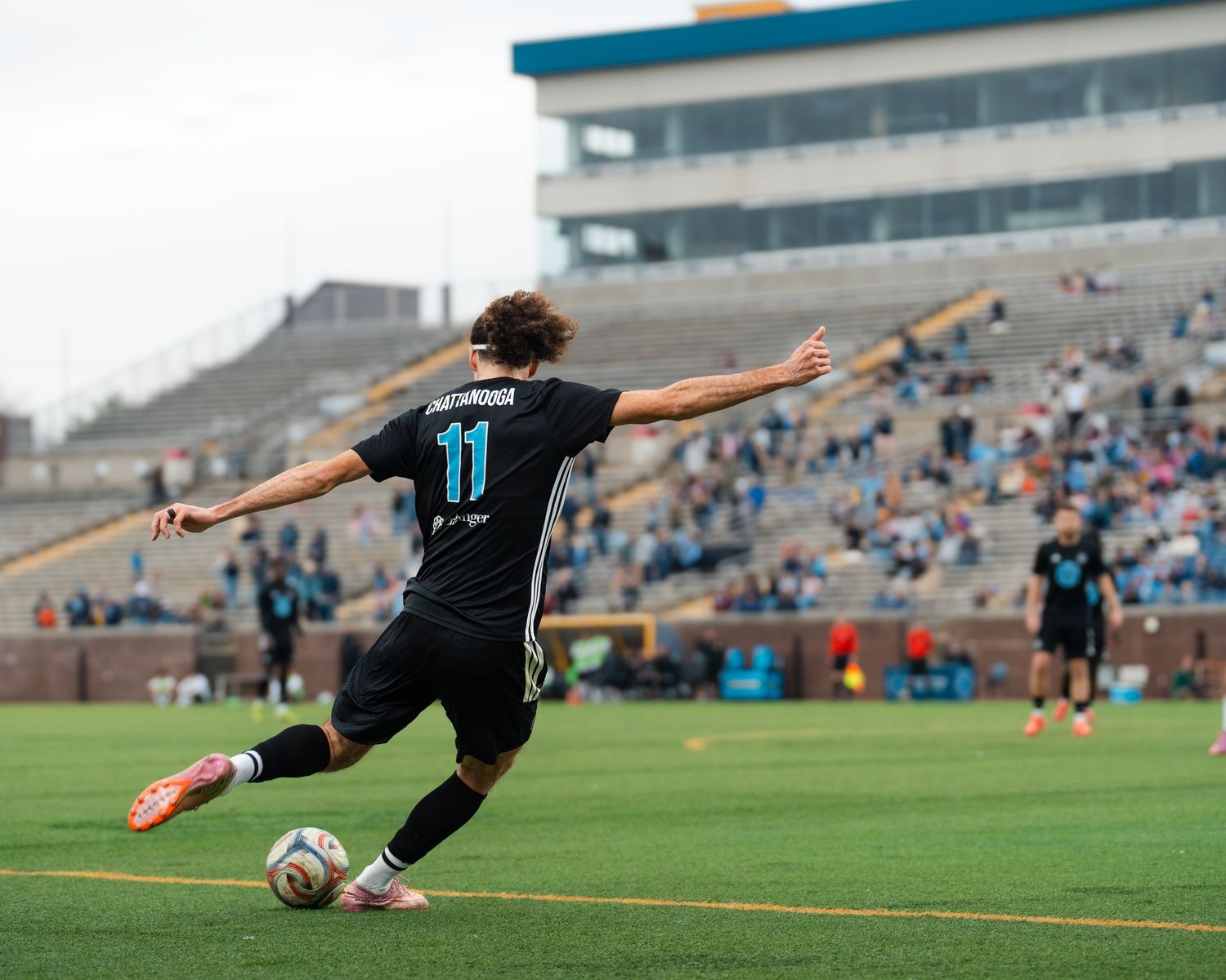 Chattanooga FC Soccer player number 11 kicks the ball during a match at a stadium filled with spectators.
