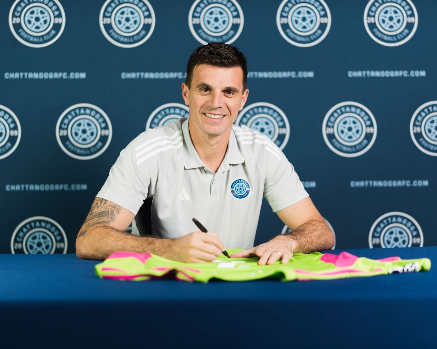 Chattanooga FC player signs contract with colorful cleats on table in front of club backdrop. Photographed for Chattanooga FC player signing
