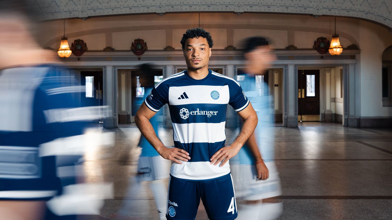 Soccer player poses in navy blue and white Erlanger jersey inside an elegant venue.