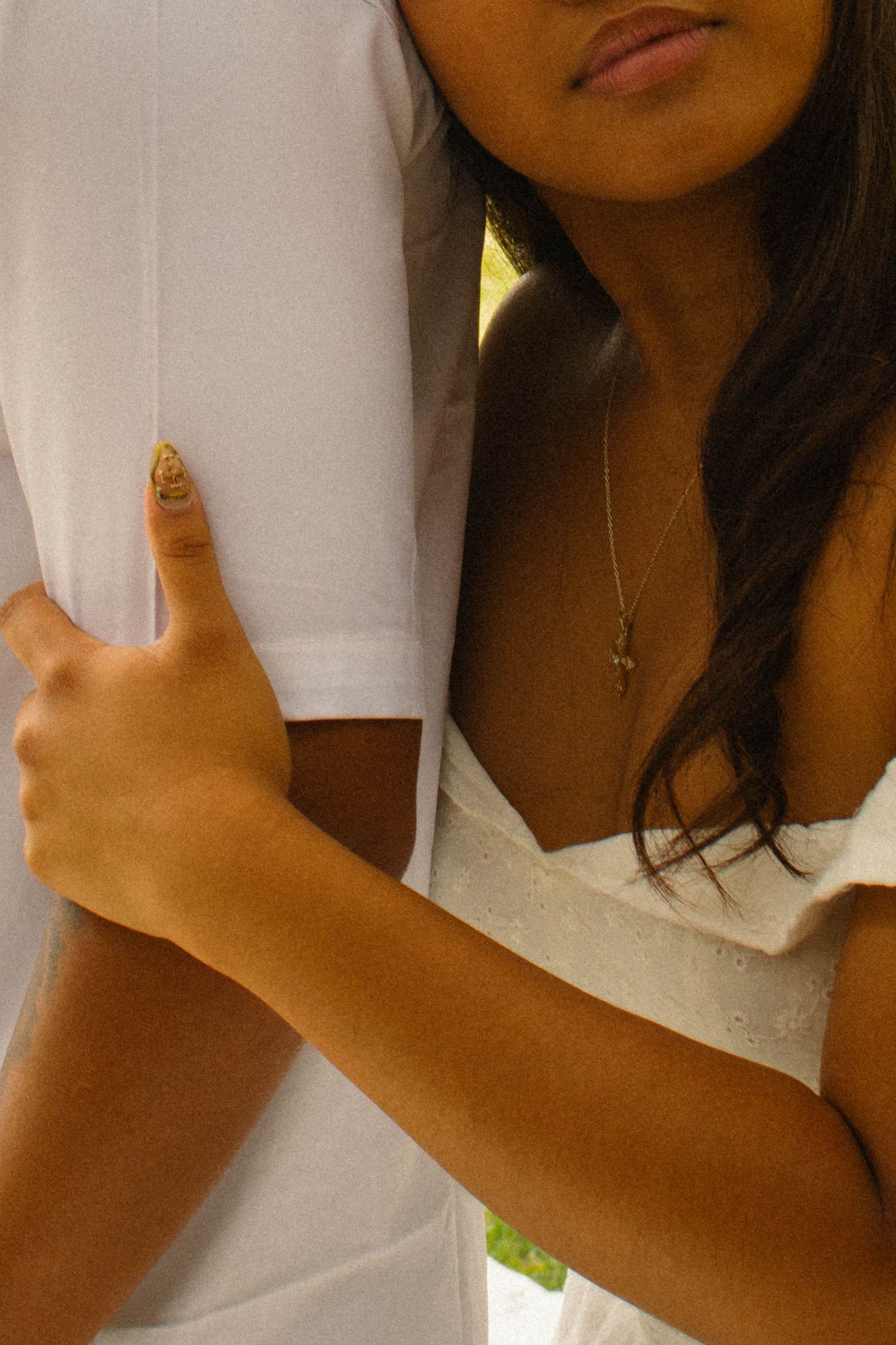 Close-up of a young woman in a white dress embracing a man in a white t-shirt, wearing a gold necklace.