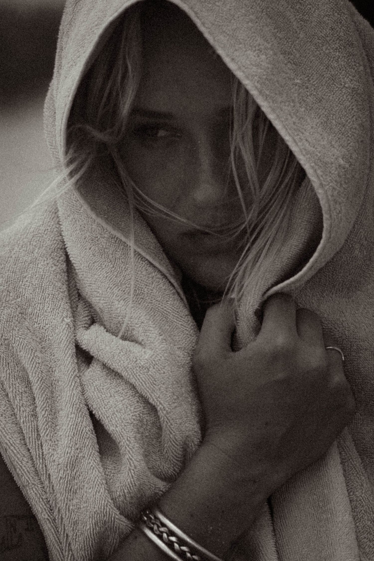 Black and white portrait of blonde woman wrapped in hooded towel gazing at camera.