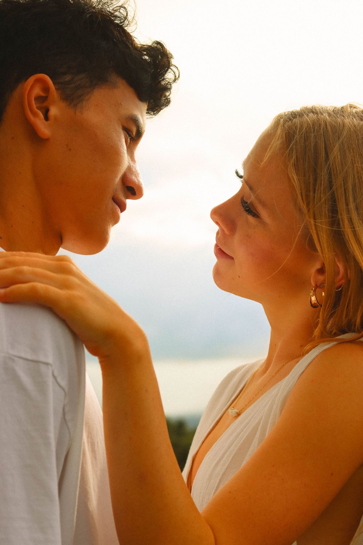 Young interracial couple gazing at each other romantically at golden hour outdoors.