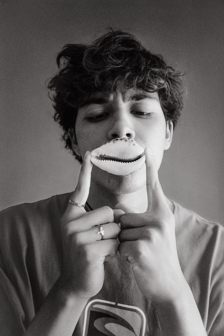 Creative black and white portrait of young man holding shell over mouth.