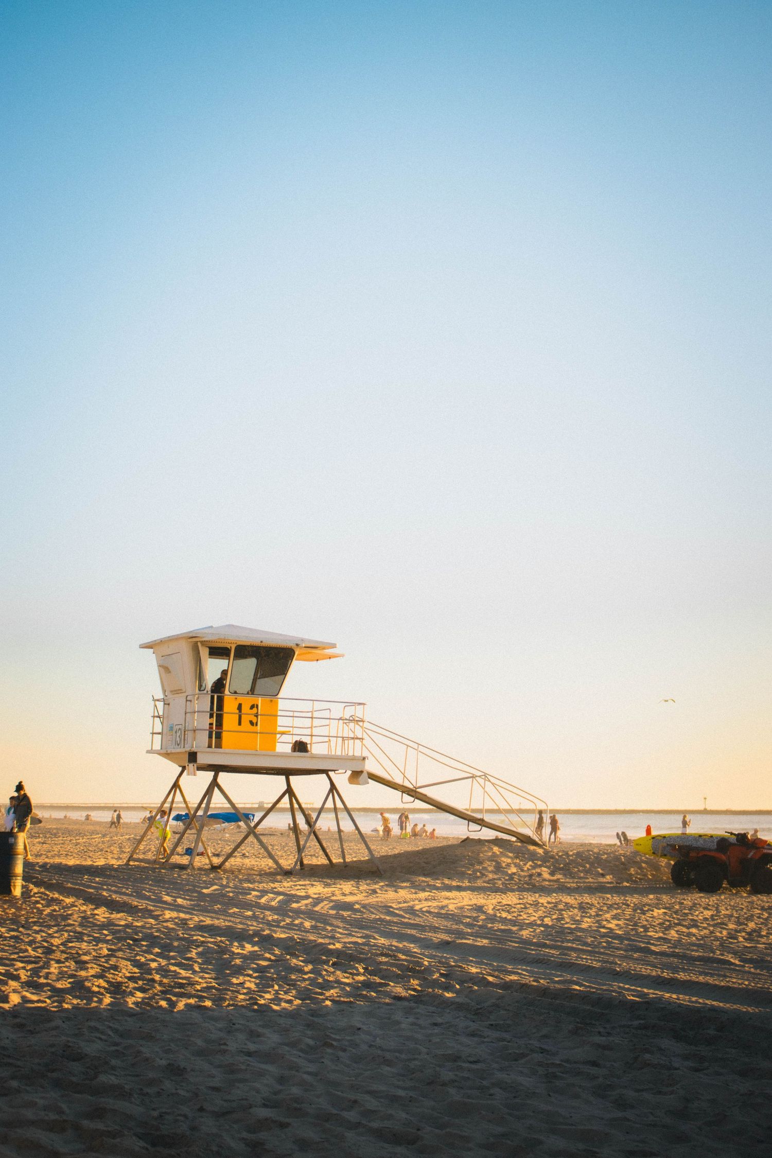 Yellow and white lifeguard tower number 13 on sandy beach at golden sunset.