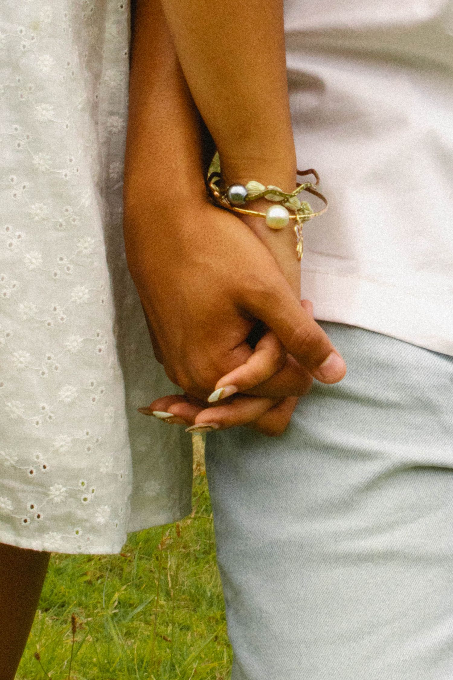 Close-up of a couple holding hands, woman wearing gold and pearl bracelets with long manicured nails.