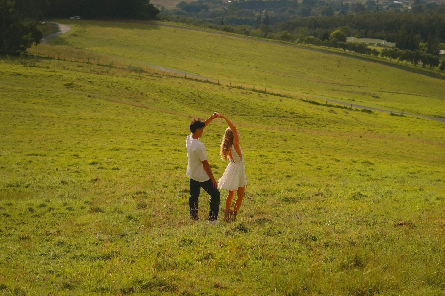 Couple dancing and spinning together in a vast green sunlit field.