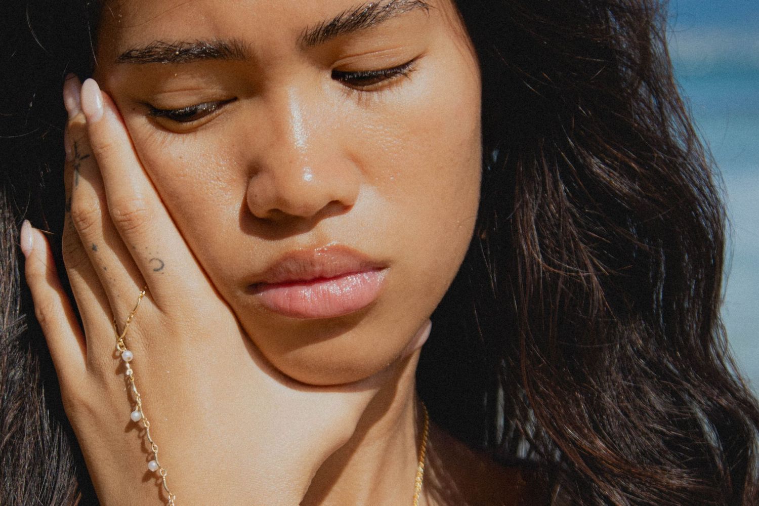 Close-up portrait of a woman with gold hand chain jewelry touching her face in sunlight.