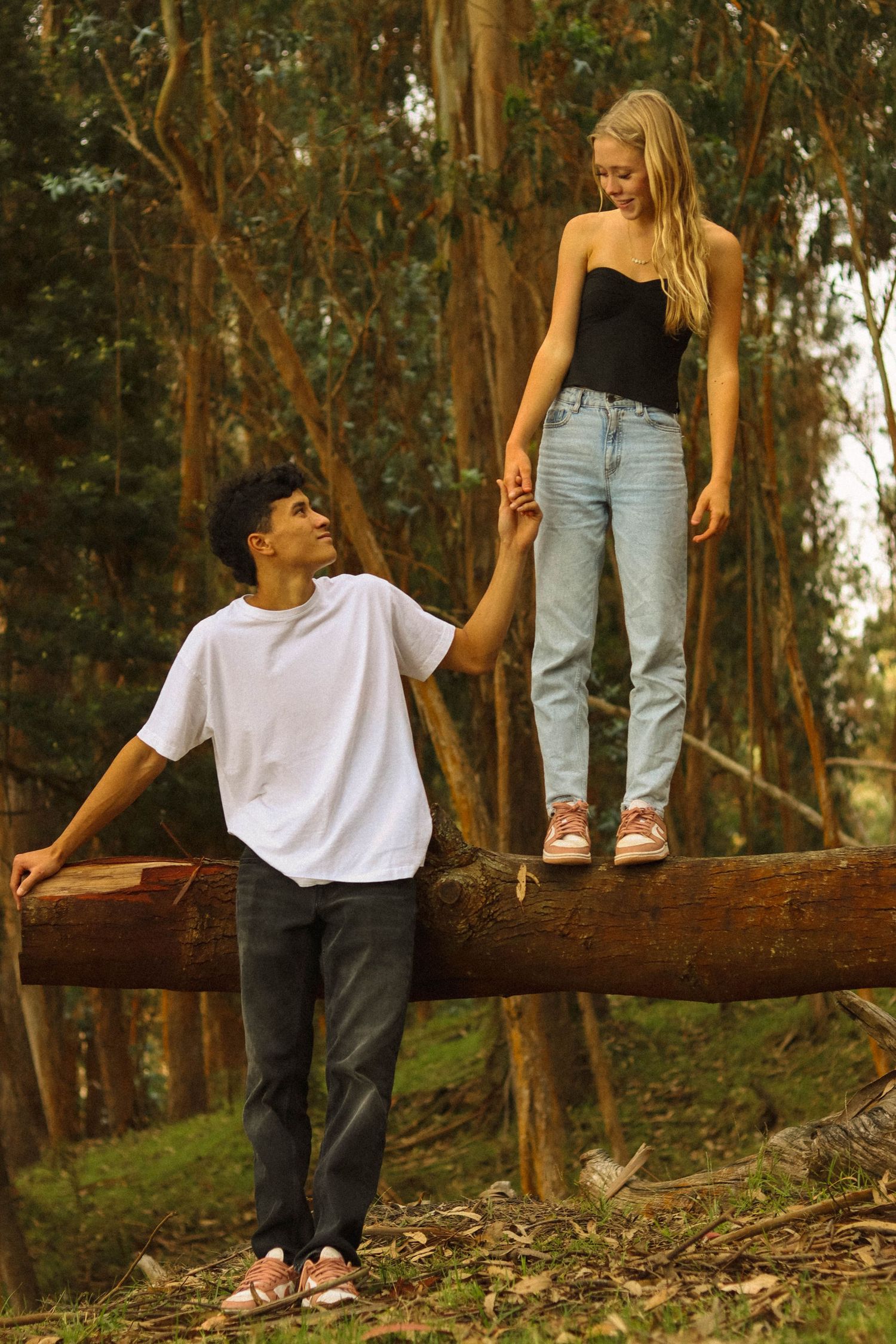 Young couple in forest, girl standing on fallen log holding hands with boy below.