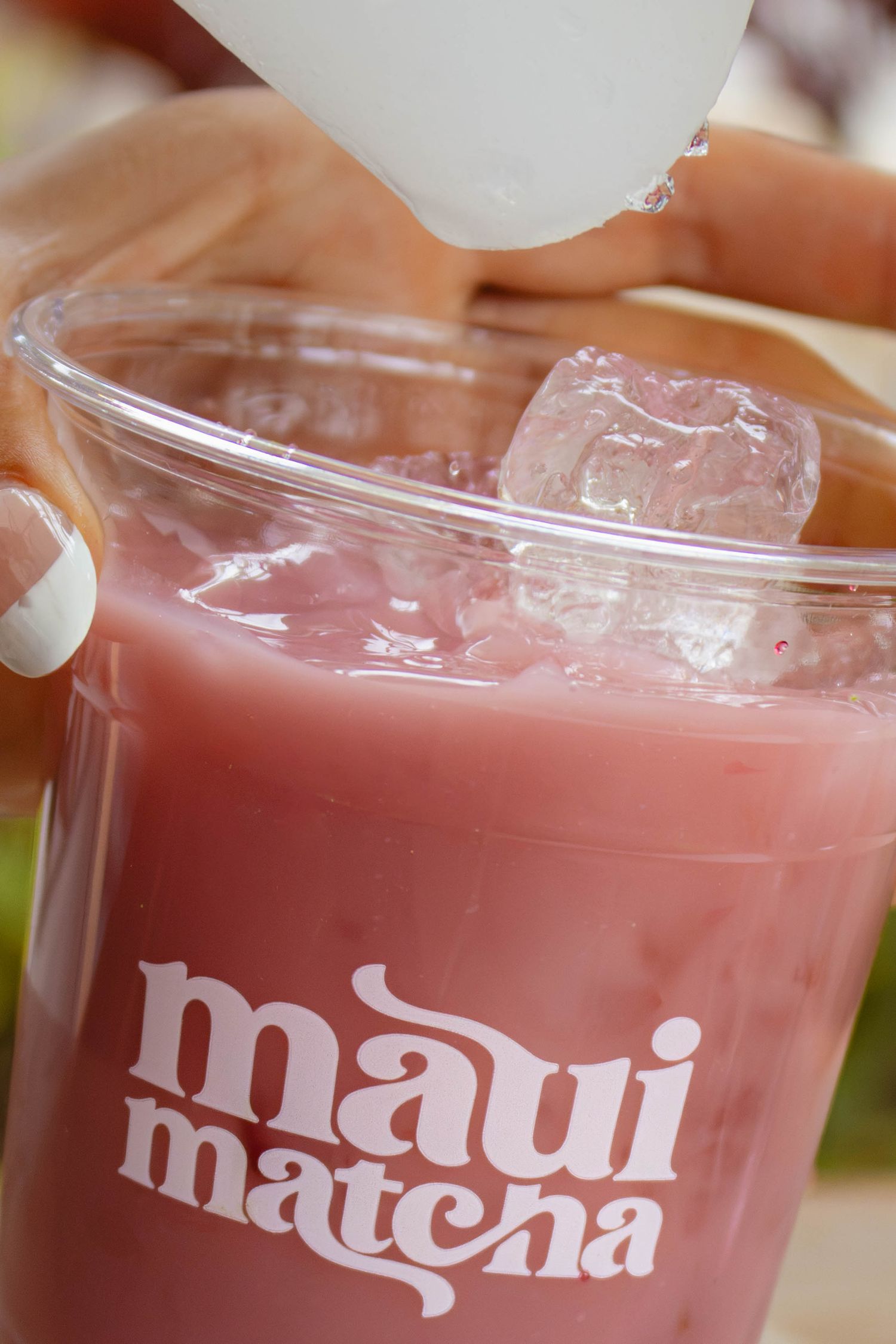 Hand pouring liquid into a pink strawberry iced drink in a Maui Matcha branded cup.