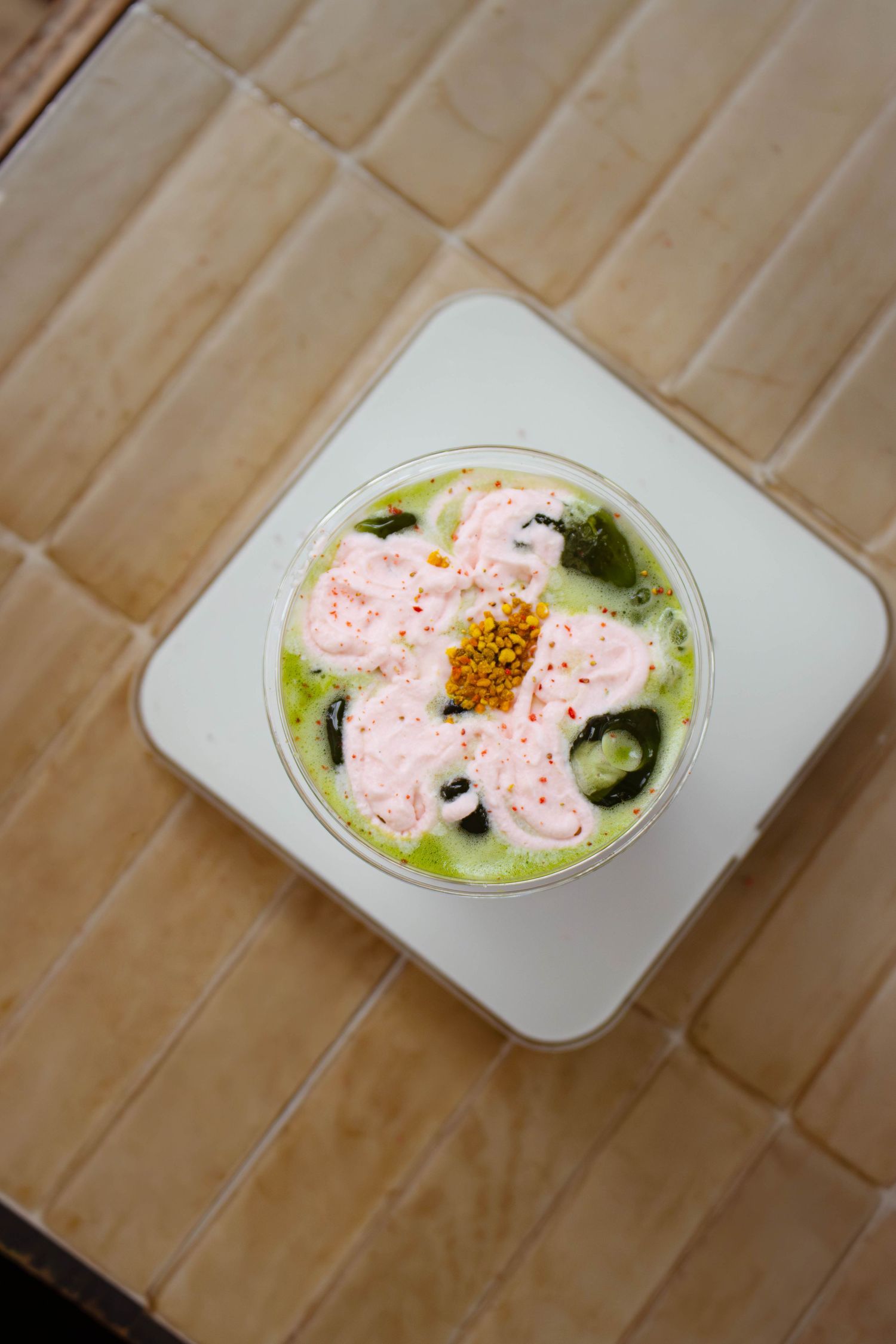 Overhead view of a matcha latte topped with pink foam and bee pollen on a white tray.