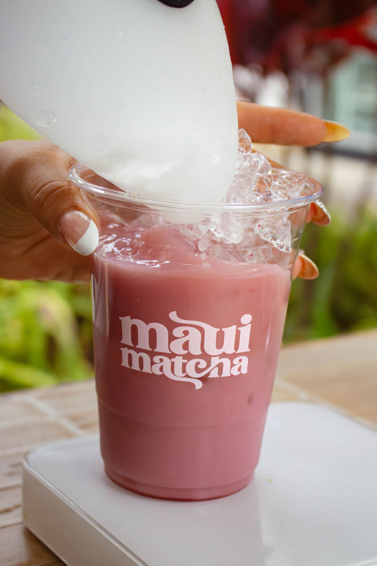 Milk being poured over ice into a pink Maui Matcha branded clear plastic cup held by a hand.