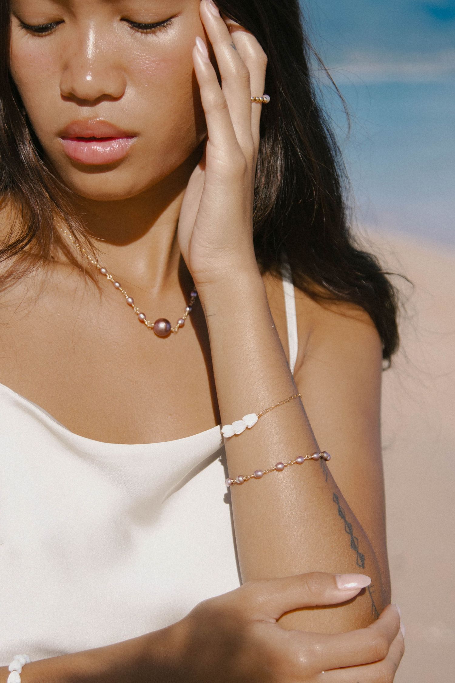 Close-up of a woman showcasing a delicate pearl bracelet and necklace set at the beach.