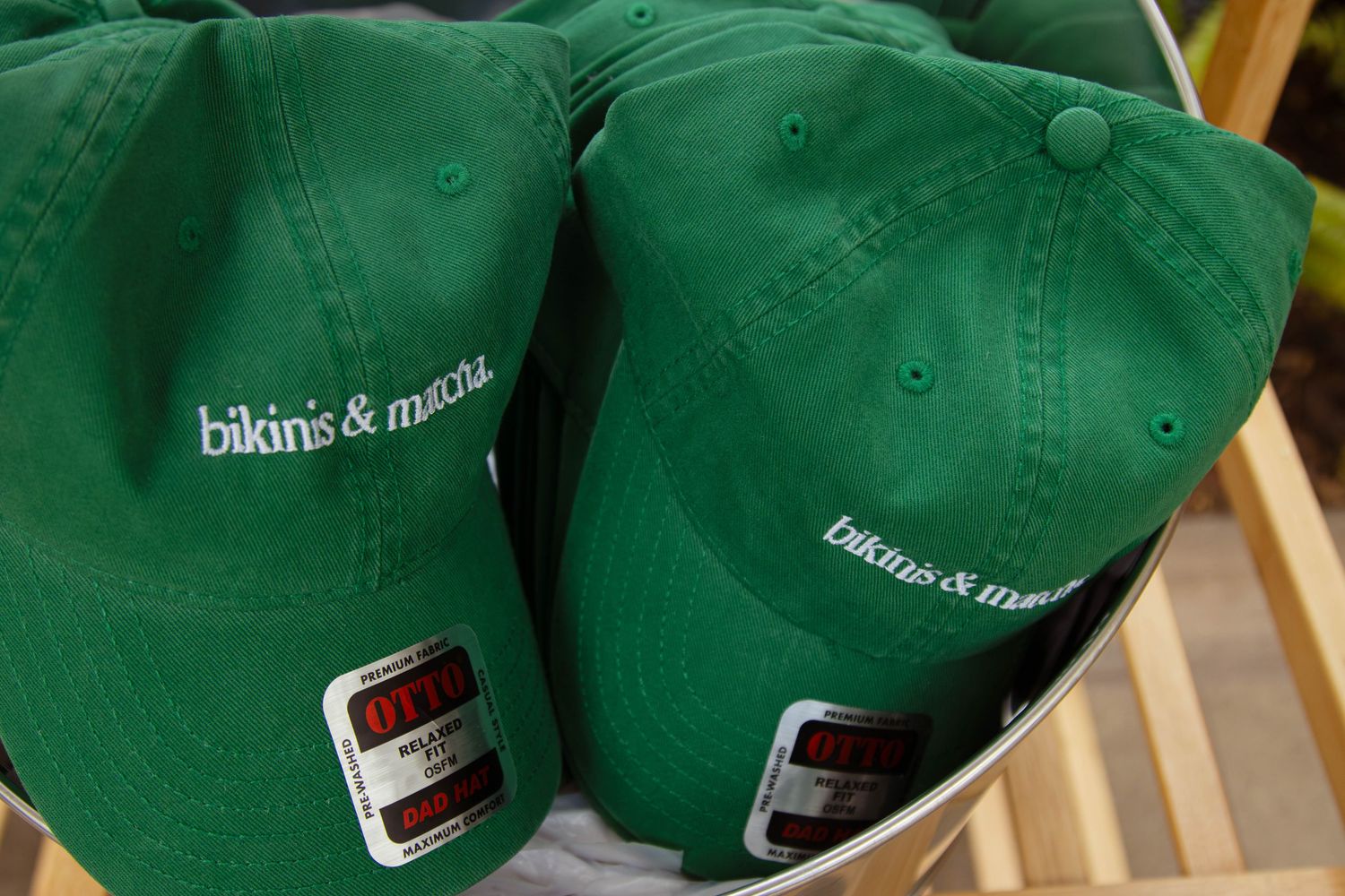 Two green baseball caps with white bikinis and matcha embroidered text displayed in a basket.