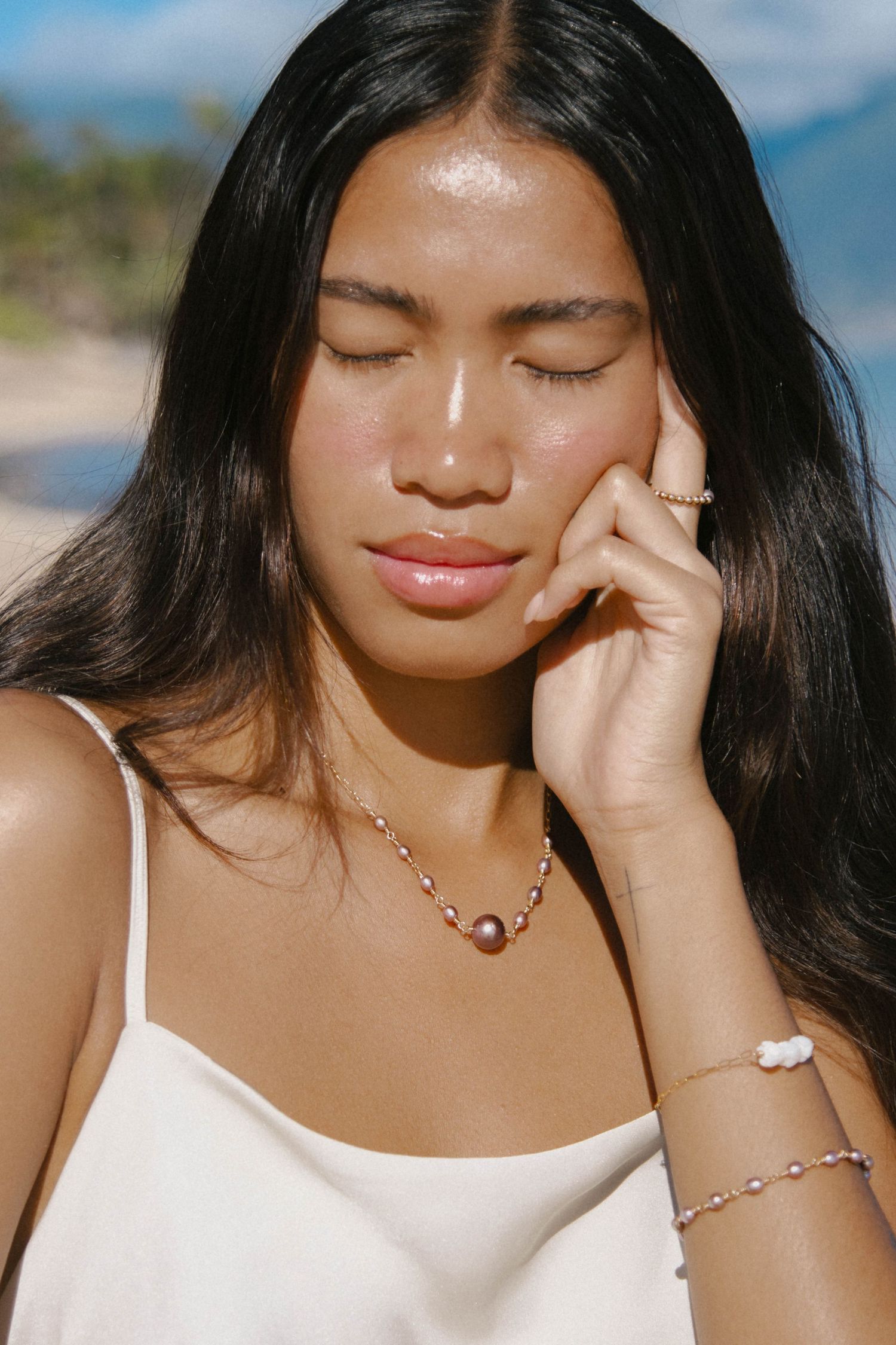 Young woman with long dark hair wearing pearl jewelry set including necklace and bracelet at the beach.