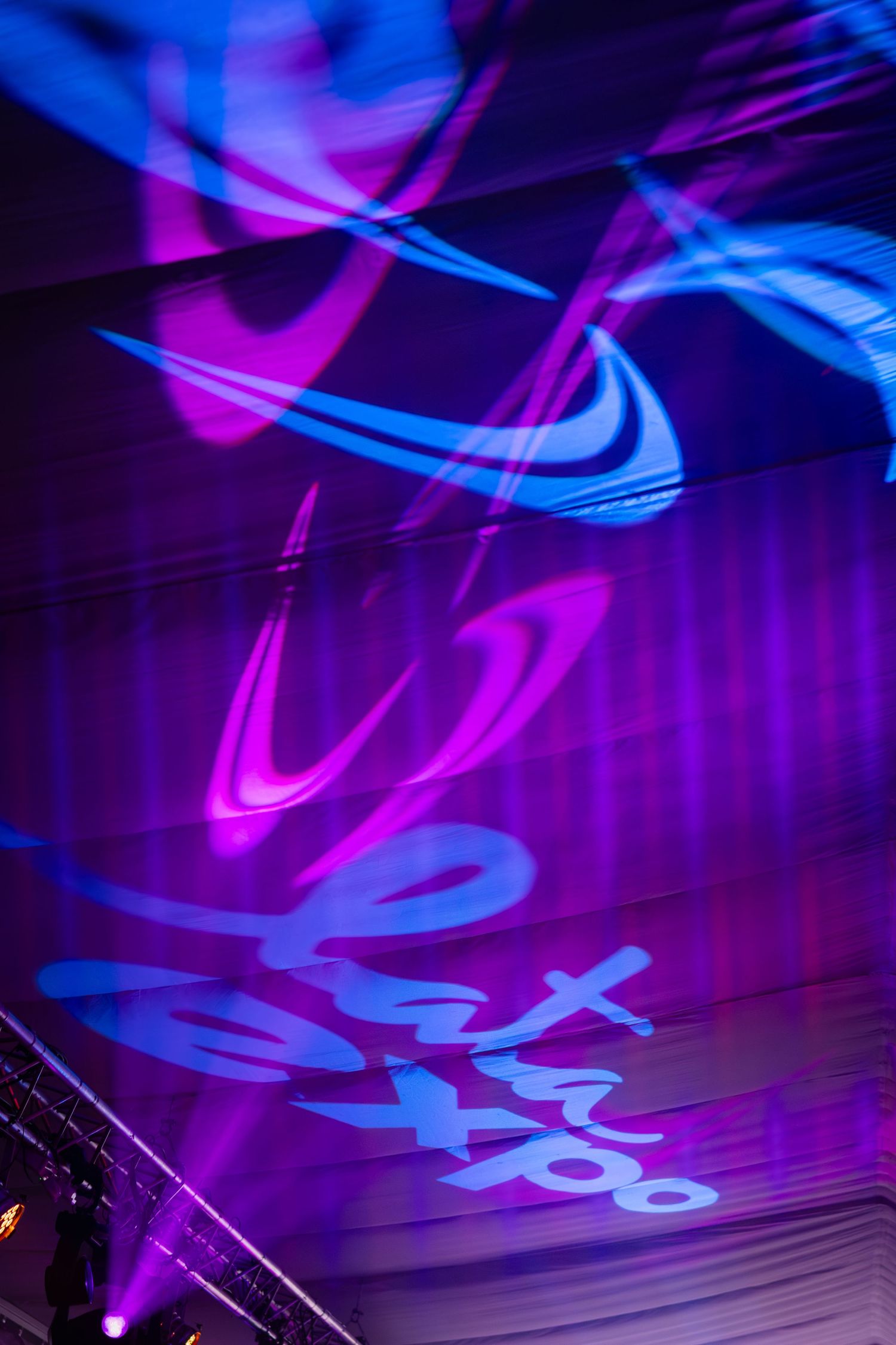 Purple and blue laser lights projecting travel expo logo on ceiling at night event.