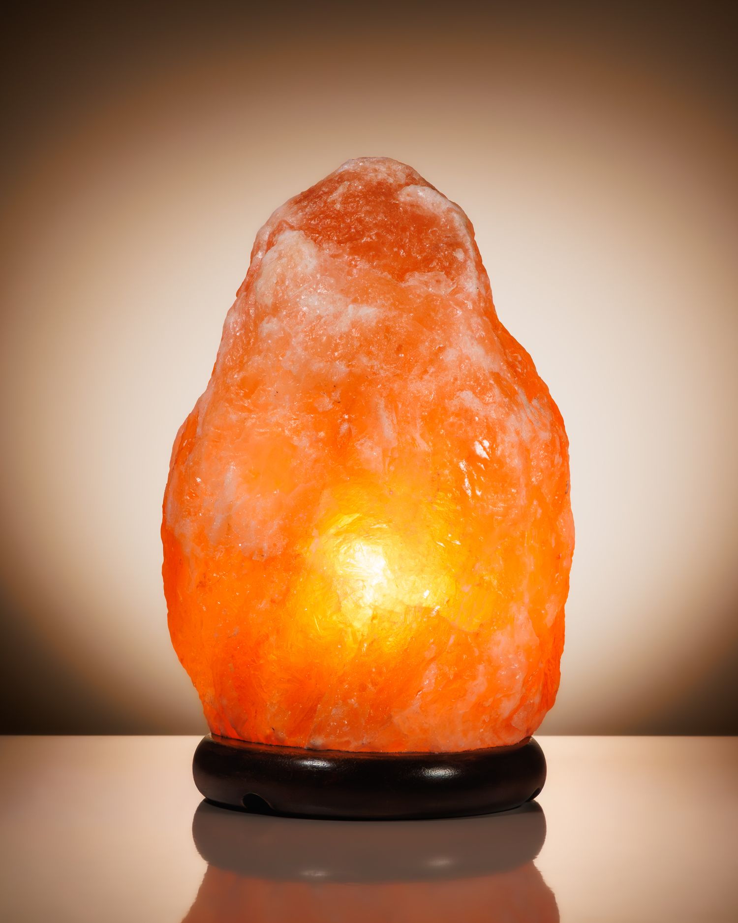 Glowing Himalayan pink salt lamp on a wooden base emitting warm orange light against a neutral background.