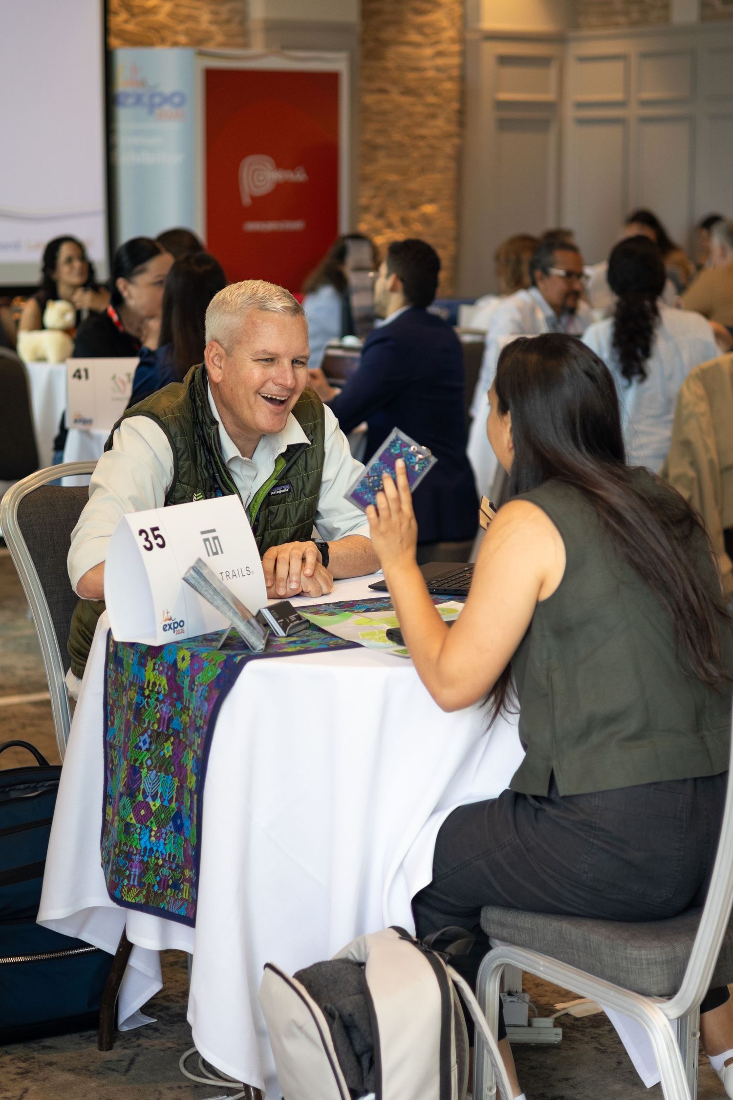 Two professionals laughing and networking at a LATA Expo business meeting table.