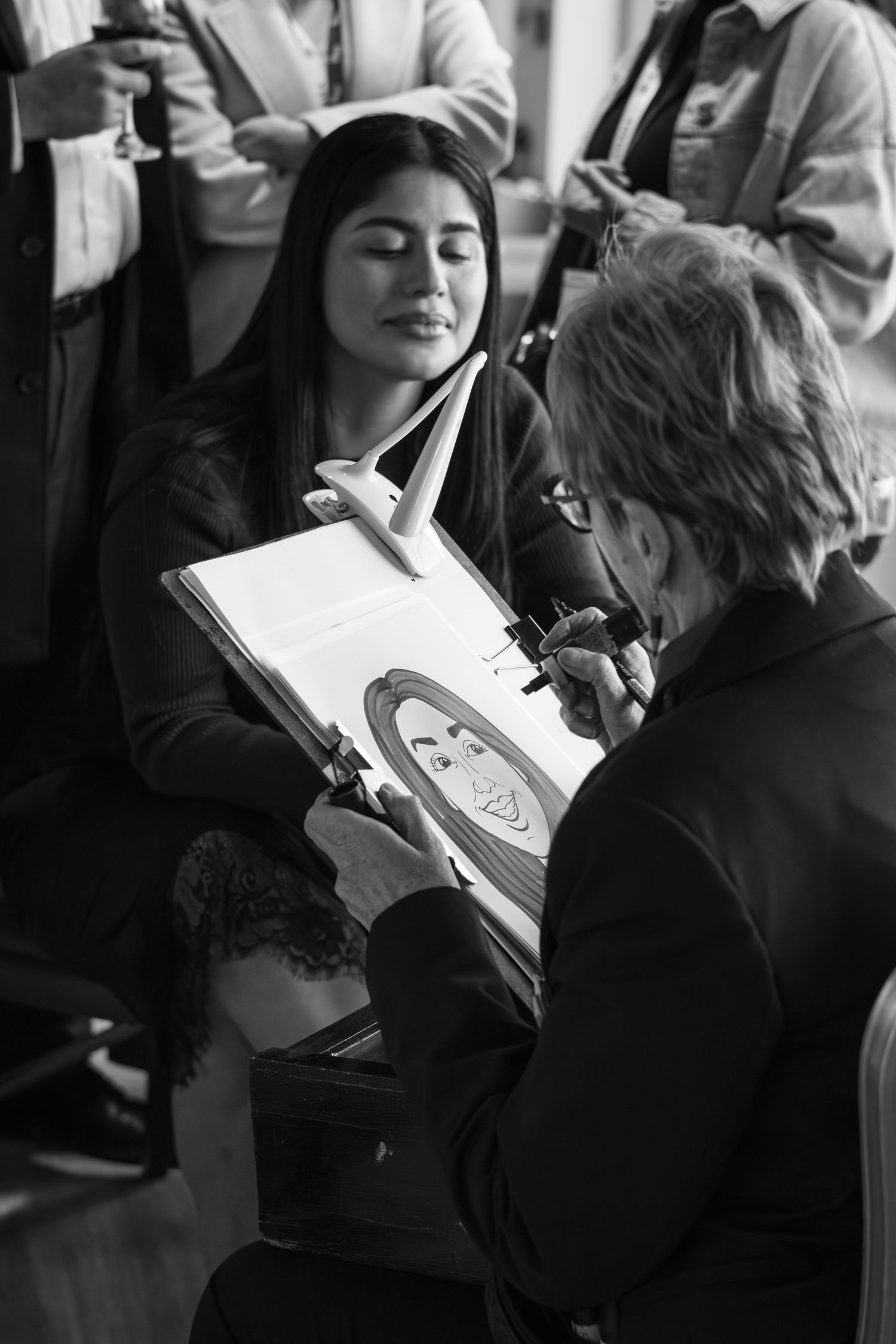 Black and white photo of an artist sketching a caricature portrait of a young woman at an event.