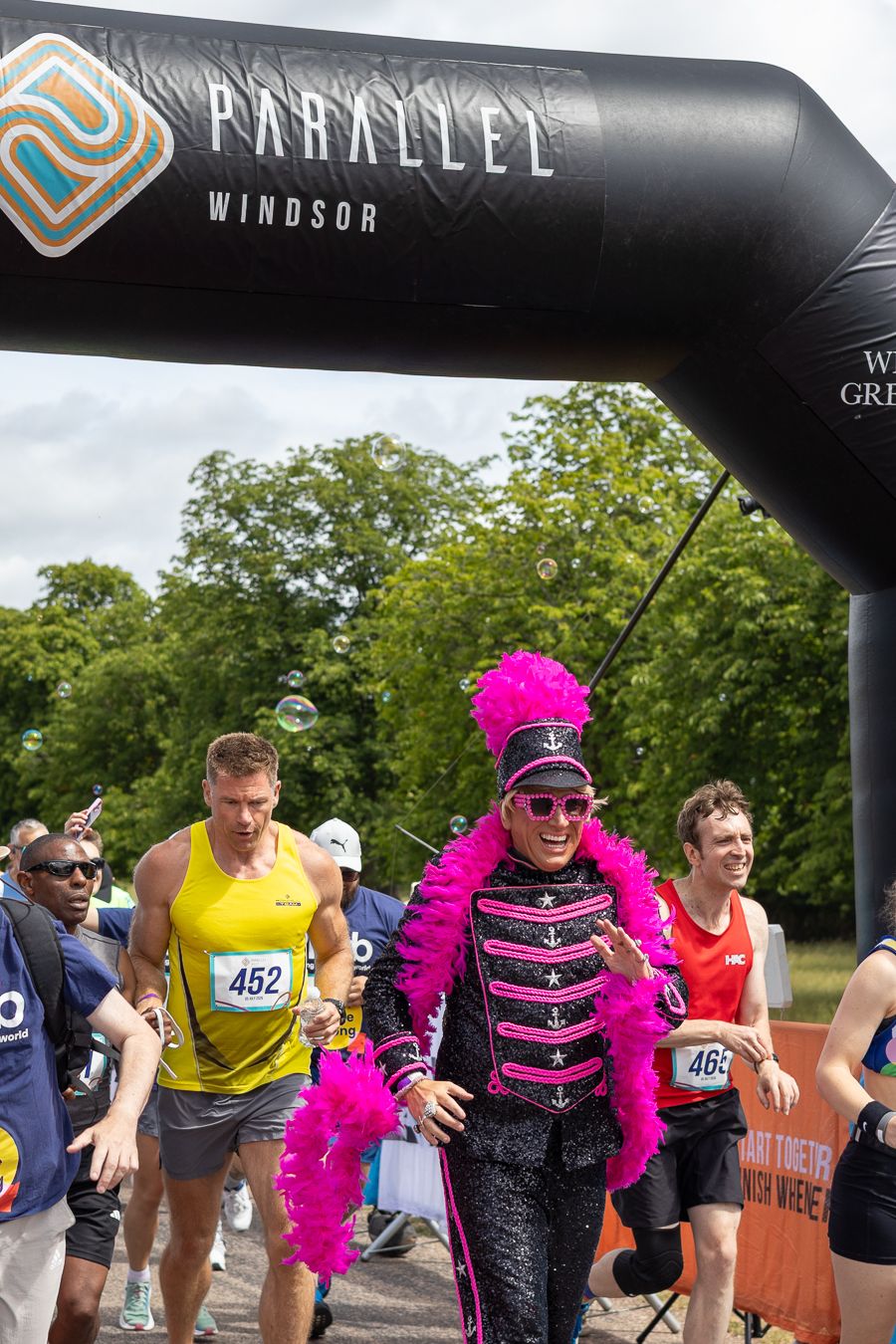 Runner in pink feathered costume crosses finish line at Parallel Windsor charity race event outdoors.
