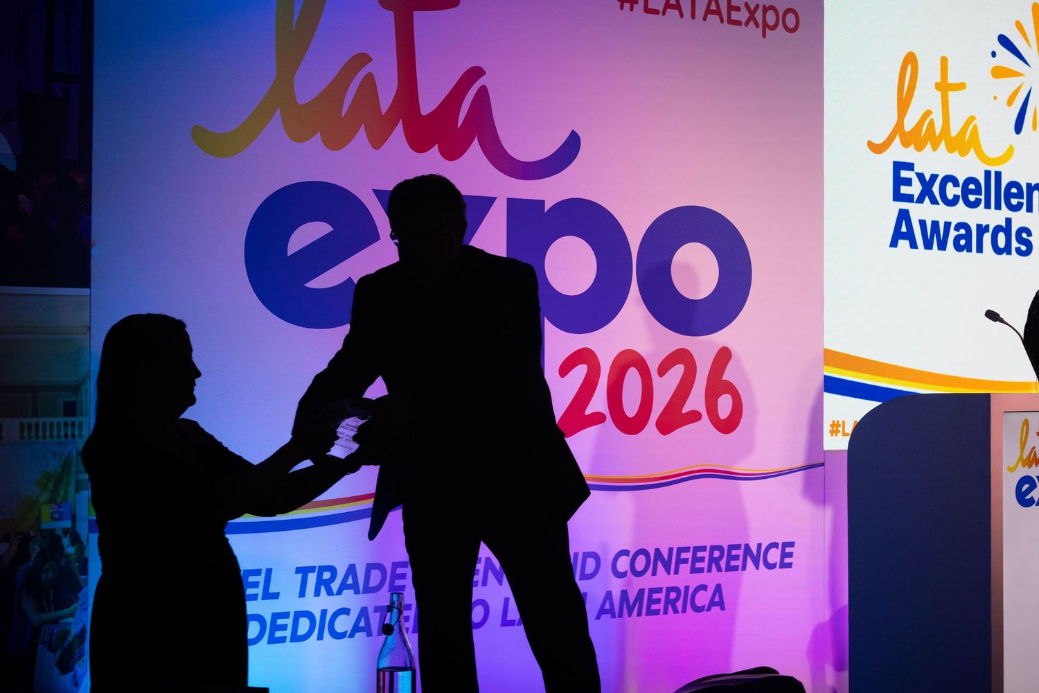 Silhouettes of two people shaking hands at LATA Expo 2026 conference stage with colorful backdrop.