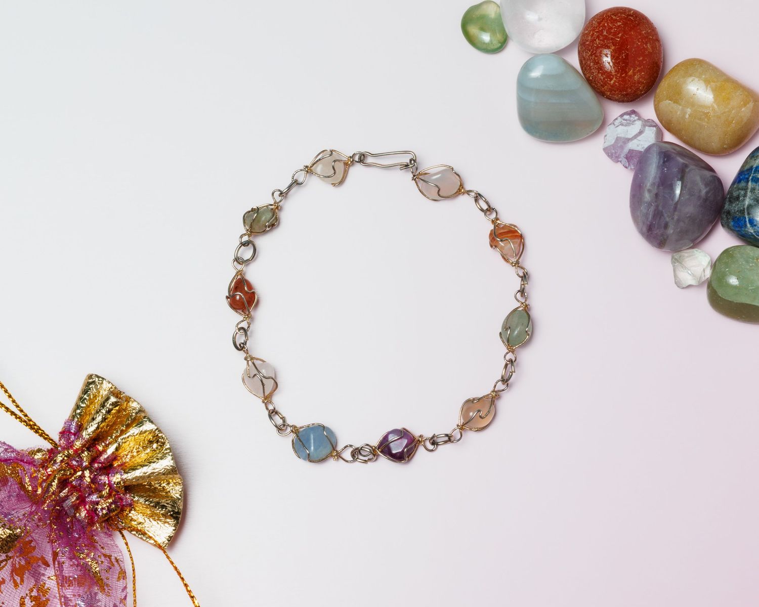 Handmade gemstone bracelet with multicolored polished stones on a silver chain, shown beside loose tumbled gems and a golden ribbon bow.