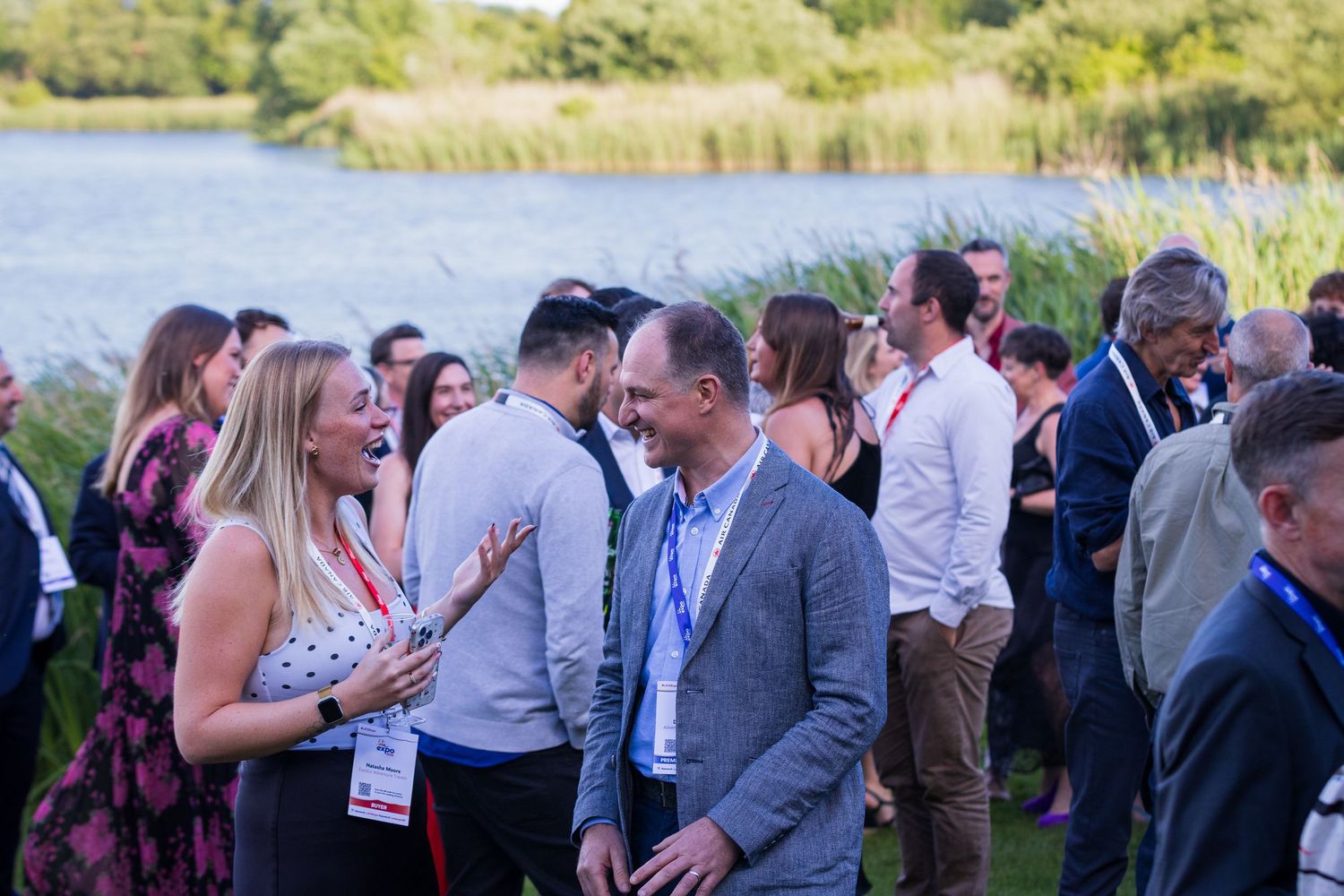 Group of professionals networking and laughing outdoors near a lake at a corporate event.