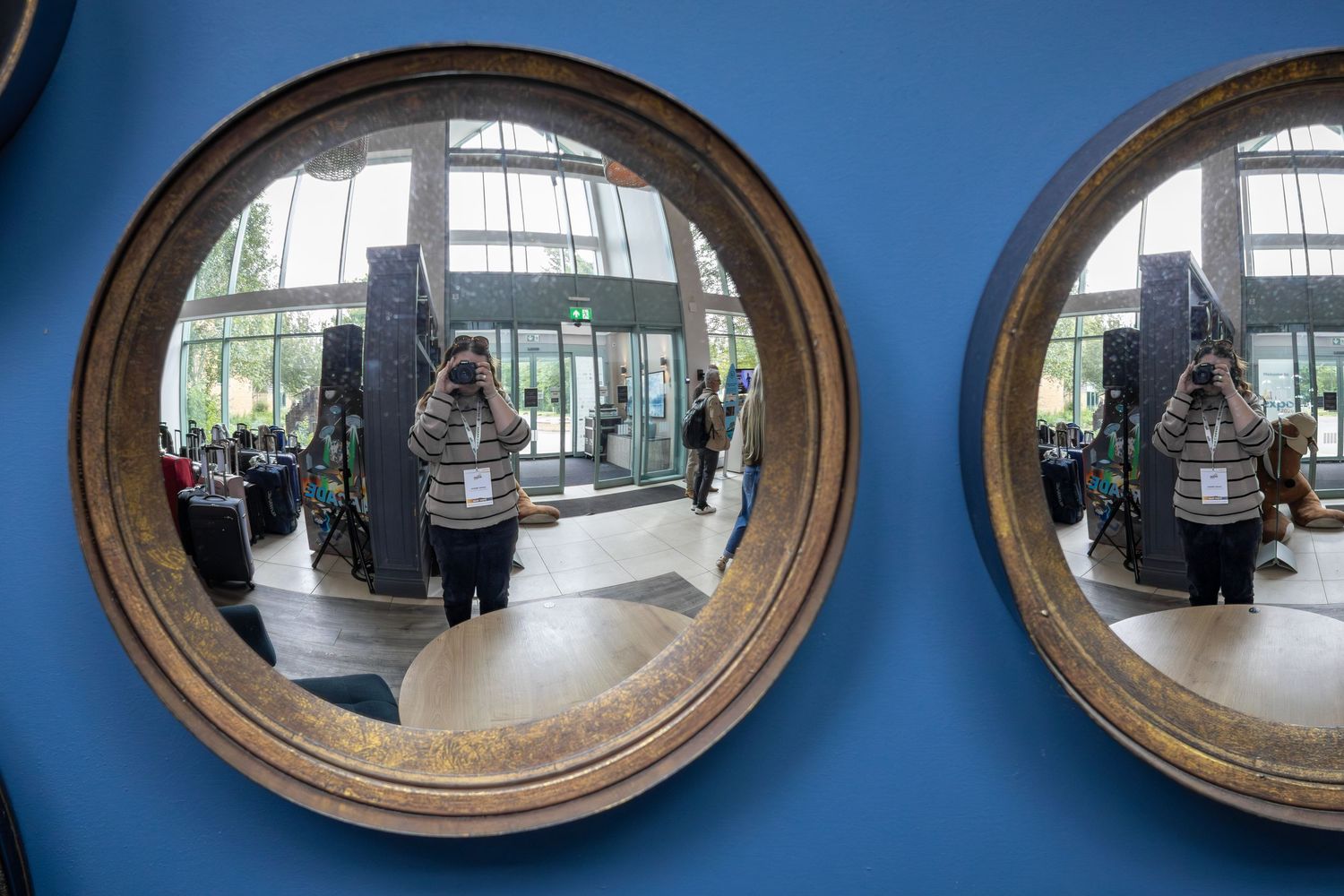 Photographer reflected in two round convex gold-framed mirrors on a blue wall.