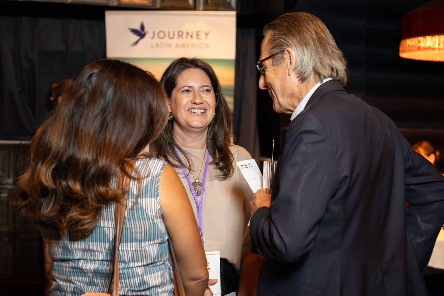 Three professionals networking at a Journey Latin America event, smiling and engaged in conversation at an indoor venue.