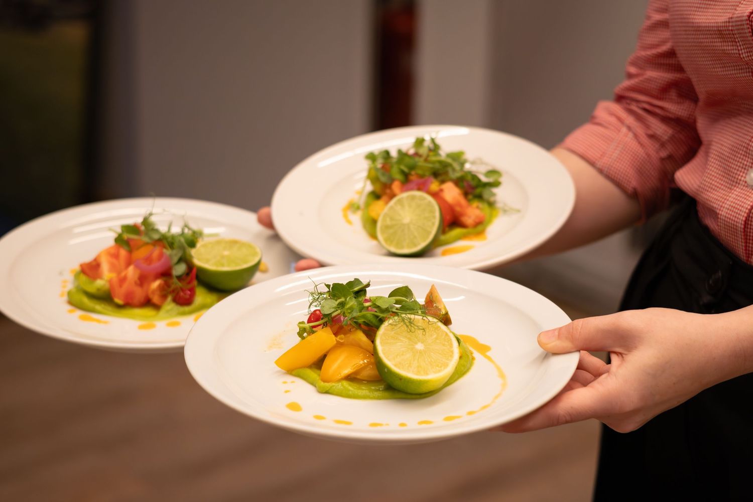 Server presenting three elegant plates of fresh salmon tartare with lime and greens.