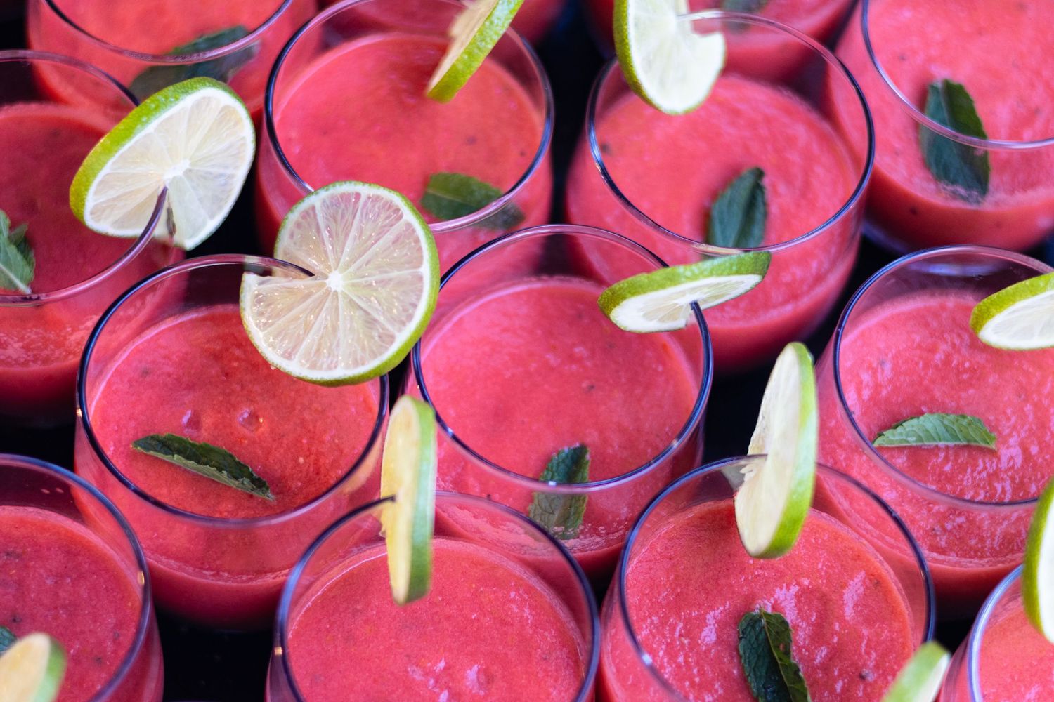 Rows of red gazpacho garnished with lime slices and mint leaves.