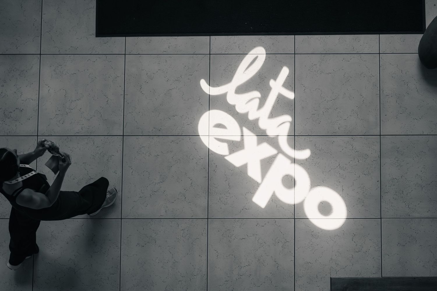 LATA Expo logo illuminated on a tiled floor with a person photographing it from above.