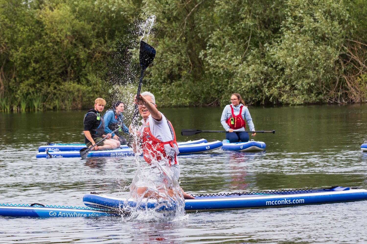 Person splashing water with a paddle while stand-up paddleboarding on a calm river.