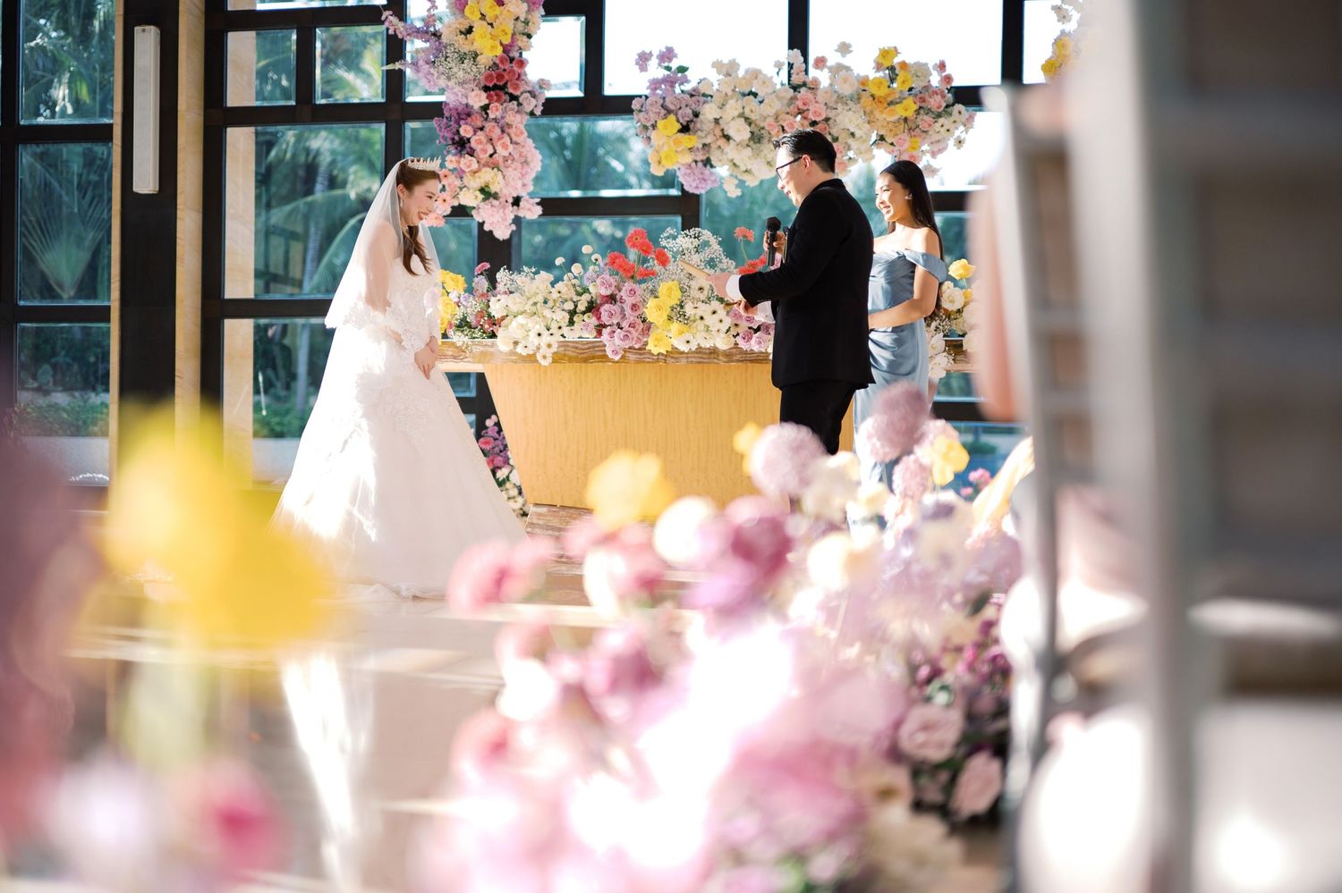 Bride and groom exchanging vows at a floral wedding ceremony with colorful pink and yellow flower arrangements.