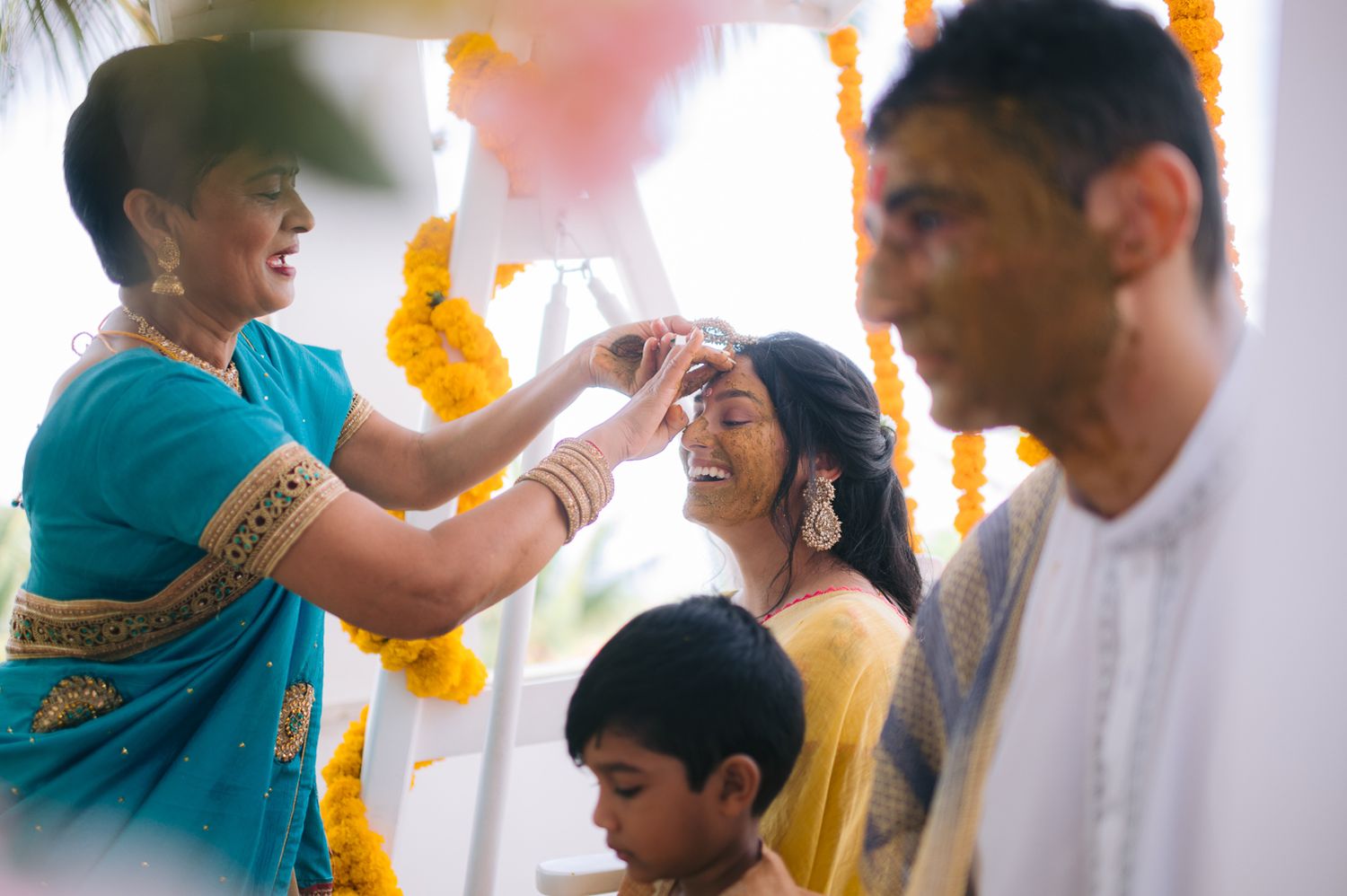 Indian wedding ceremony with women in colorful saris sharing joyful moment, yellow marigold garlands decorating the mandap.