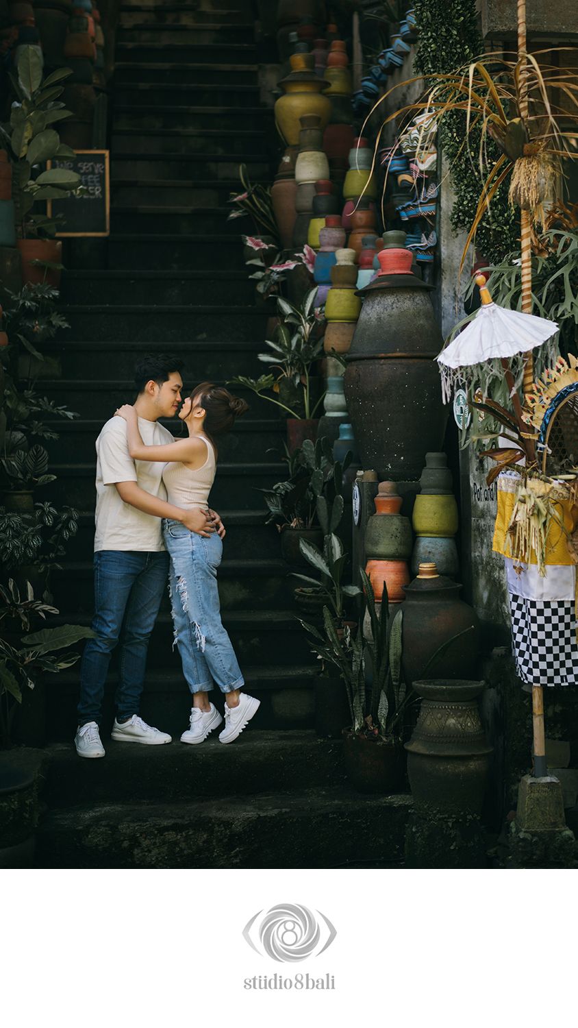 Couple embracing on stone steps surrounded by colorful pottery and tropical plants in Bali.