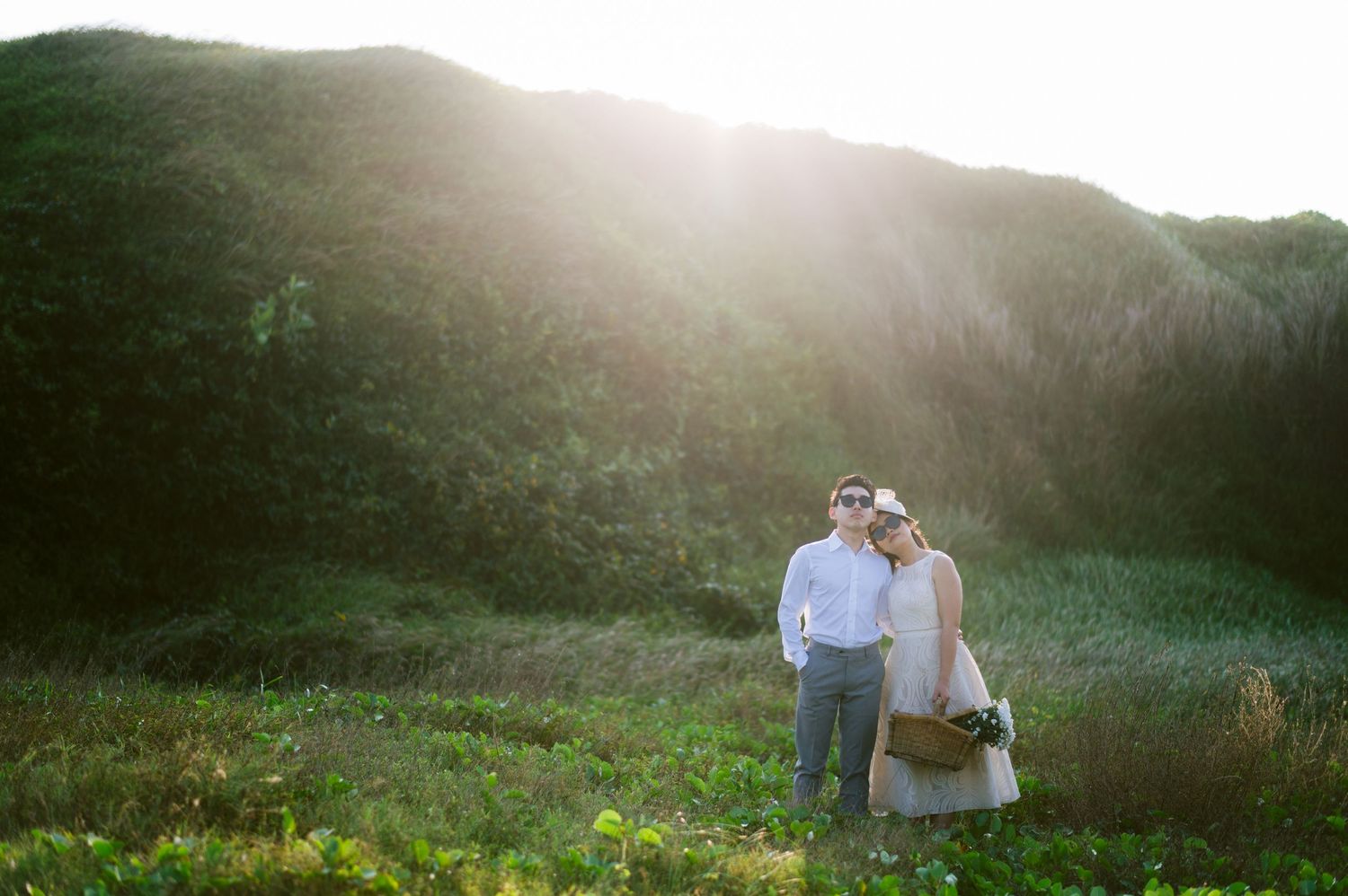 Couple embracing in a sunlit green meadow with golden backlight, perfect for romantic outdoor wedding photography.