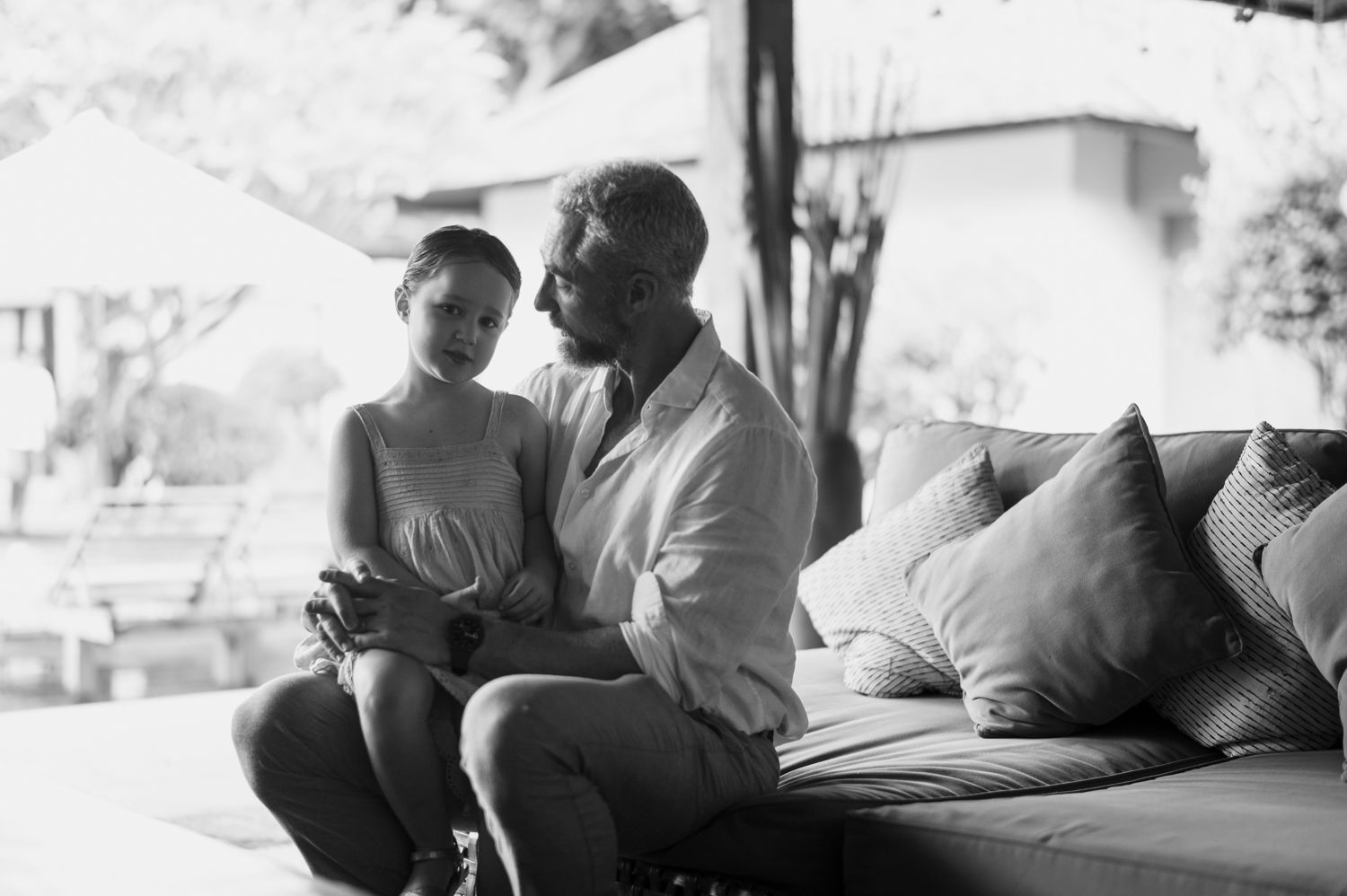 Black and white photo of a father and child sitting together on a couch, sharing a tender moment.