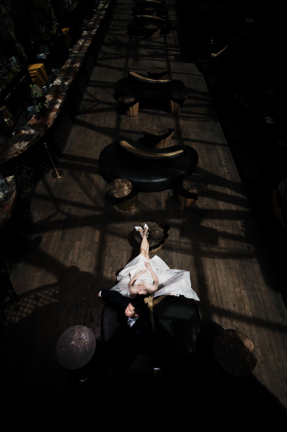 Aerial view of a bride and groom dancing in dramatic shadows on a dark wooden floor at their wedding reception.